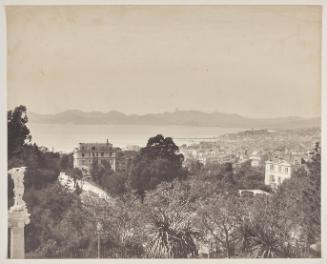 View from the hillside above Cannes looking towards the coastline.  'La jetée Edouard VII en construction'  Two villas in the middle ground.  A sculpture of St. George slaying a dragon on top of a pedestal with an Ionic capital to the extreme left.