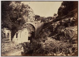View of a mountain gorge with a small building below a road bridge.
