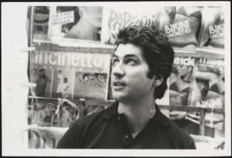 Portrait of the homosexual poet Dario Bellezza standing in front of magazines.