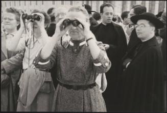 Clergymen stand in St. Peter's Square behind women with binoculars