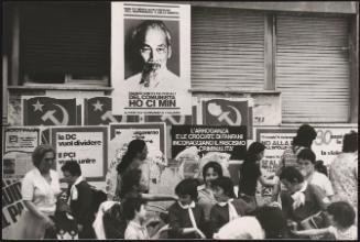Children and mothers walking past a wall covered in communist posters including a poster of Vietnamese leader Ho Ci Min