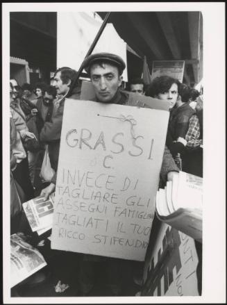 A man hands out protest papers and holds a placard with a message against cutting child benefits



