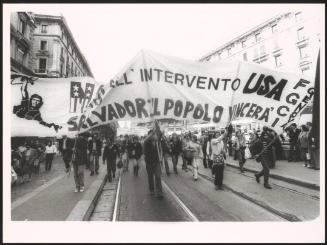 Milan 1982. A crowd of protesters march holding up a large banner down a street at a communist  peace march for the P.C.I