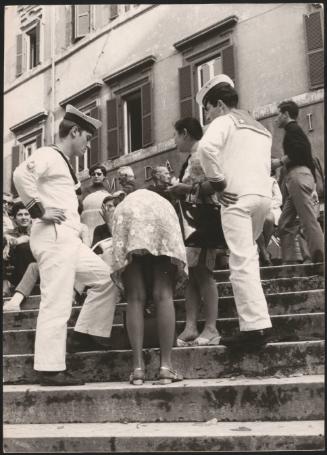 A woman flanked by two sailors bends over on some steps
