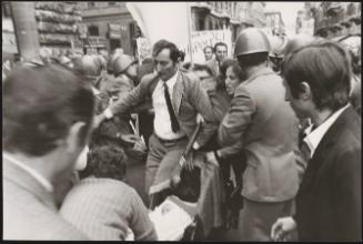 A woman tries to take a baby in a pushchair through a protest and riot police
