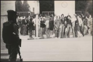 An armed guard watches as crowds gather across the street