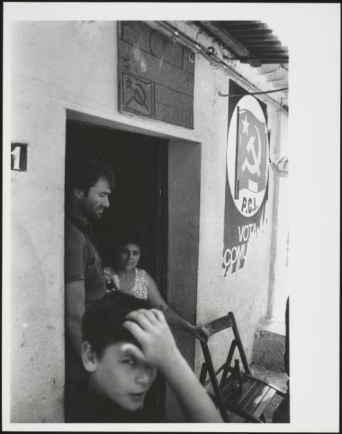 A family stand in the doorway of their home. Communist Party posters hand outside