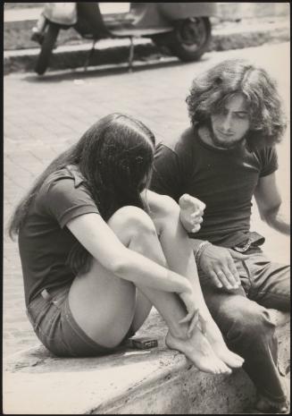 An Italian 'Pappagalli' man sits with a female tourist on a curb