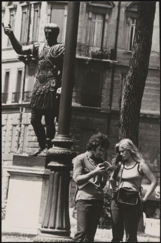 An Italian 'Pappagalli' man helps a female tourists consult a guide underneath a statue of Julius Caesar, Rome
