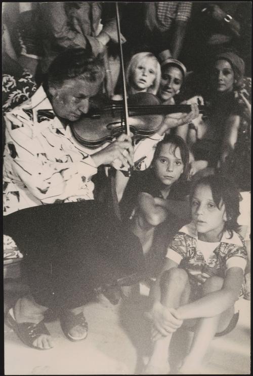 A Romani woman plays a fiddle to a group of children