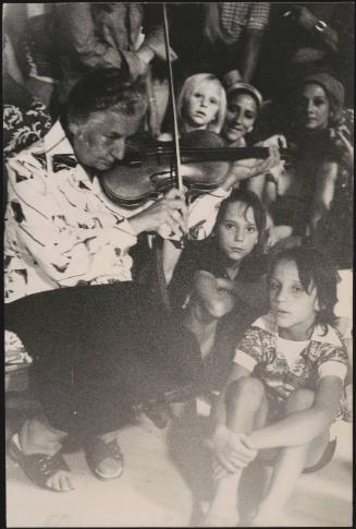 A Romani woman plays a fiddle to a group of children