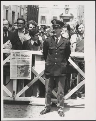 A policeman guards barriers with crowds behind him and the front page of the Christian Democracy newspaper, Il Popolo, bearing a large image of Aldo Moro pinned to it