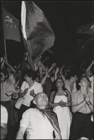 A crowd of PCI supporters cheering and waving flags underneath the headquarters building in Rome