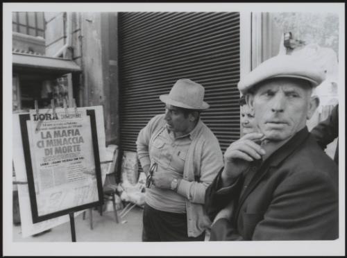 A small crowd gathers around a newspaper with an anti Mafia headline