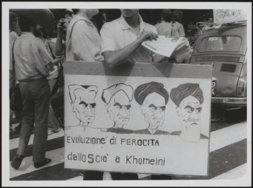 A young man wears a protest placard around his neck with cartoons of Iranian leader Khomeini