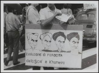 A young man wears a protest placard around his neck with cartoons of Iranian leader Khomeini