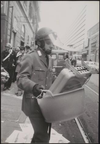 A policeman wearing riot gear carries out squatters' belongings after a forced eviction from the building in the background at the left of the picture