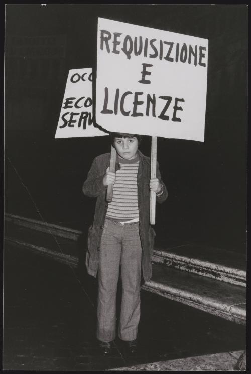 A young boy holds a protest placard that reads "Requisizione e Licenze"