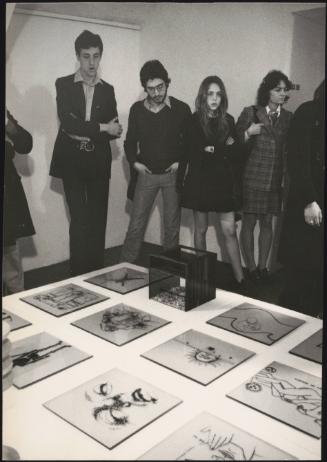 Young people at a gallery opening looking at artworks displayed on a low plinth