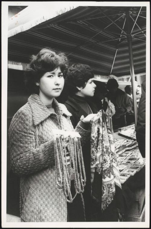 Two young women sell strings of beads and scarves at the market
