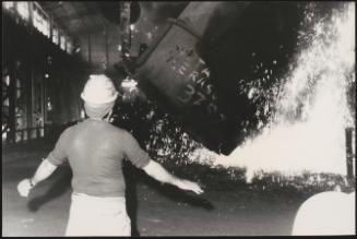 A factory worker stands back as sparks fly from machinery on the factory floor