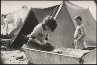 A young girl washes an item of clothing on  a washboard in a refugee camp after the destruction of the Belice earthquake in Sicily 1968