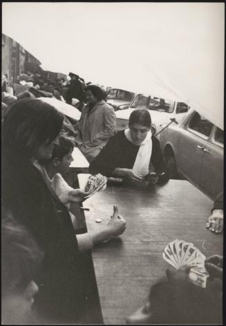 Survivors of the 1968 Belice earthquake play cards and commune at tables under temporary shelter on the streets