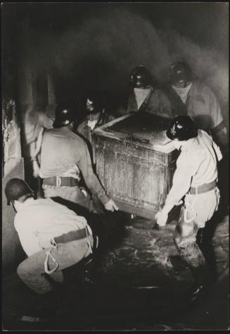 A team of policemen with their faces covered carry a heavy chest during the Belice earthquake rescue, Sicily 1968