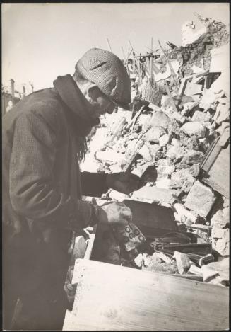 A survivor of the Belice earthquake looks through the rubble of destroyed homes, Sicily 1968