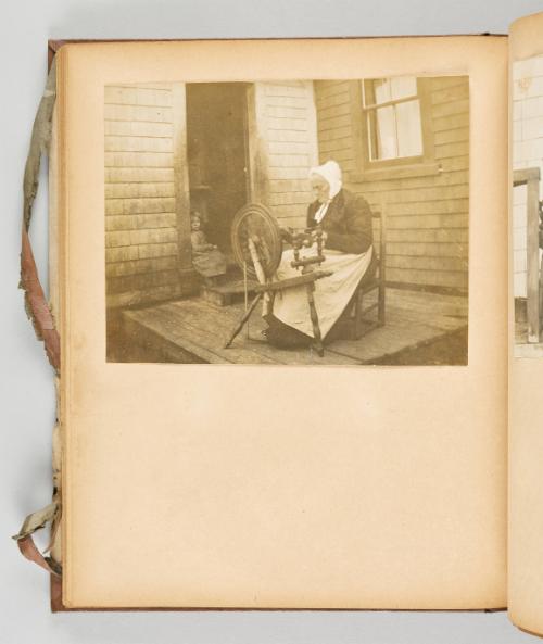 [Older woman on the porch at her wheel while a child sits in the doorway] [Page 49 of Quebec I; from collection of Canadian albums compiled by Edith S. Watson, 1890s-1930s]