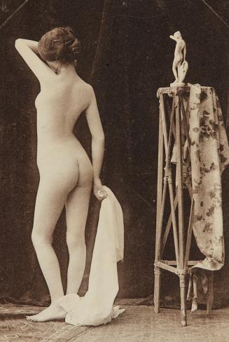 [Standing woman striking pose of sculpture on stand, back view]