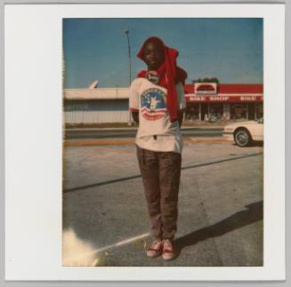 [Boy standing in parking lot with red sweater wrapped on his head]
