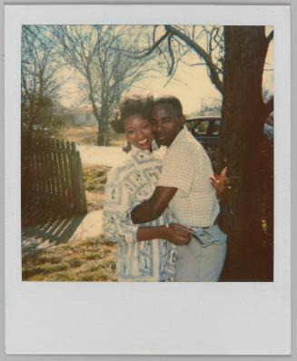 [Man and woman hugging outdoors, woman had long red nails and is holding polaroids]
