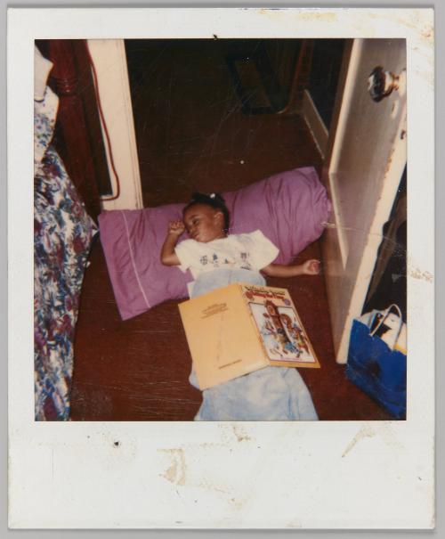 [Little girl sleeping on ground with blanket and pink pillow]