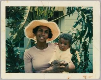 Pamela & Mauricee Noel, Age 4 Months [Woman in straw hat holding baby in front house]