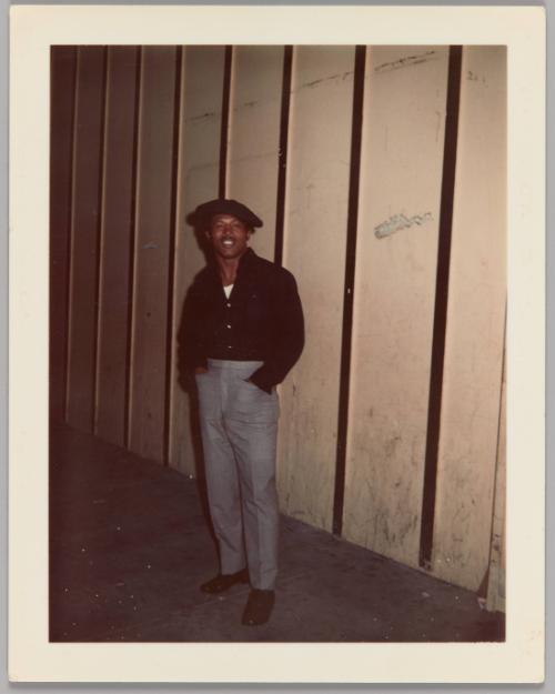 [Man posing in front of paneled wall, wearing black beret]
