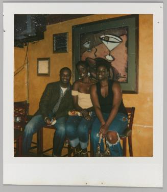 [Man and two women posing on stools, martini painting in background]
