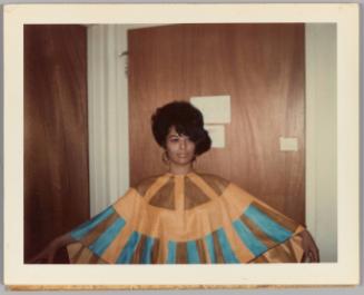 [Woman posing in front of wood door, wearing blue and tan cape dress]
