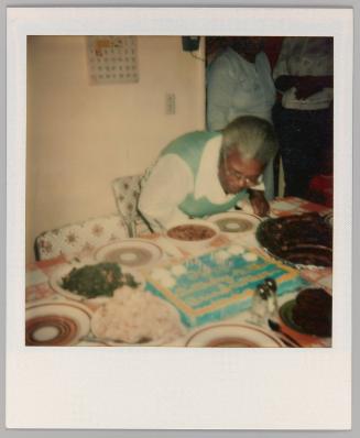 [Woman leaning over dining table with sheet cake on top]
