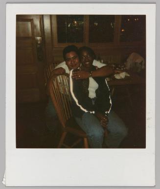 [Young man embracing woman from behind seated at dining table]
