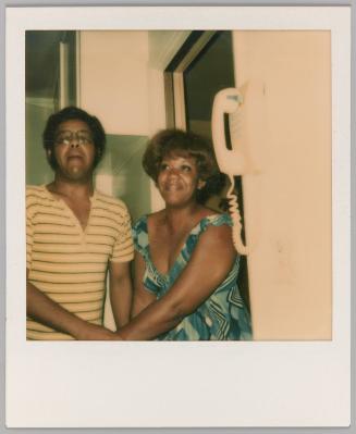 [Man and woman holding hands with white telephone on wall]
