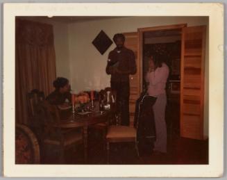 [Two women and man in dining room having a conversation standing 
