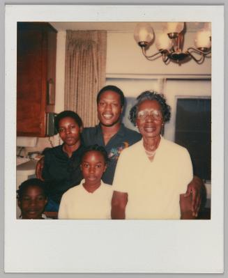 [Elderly woman, man, woman and two children pose in home with light fixture in background]
