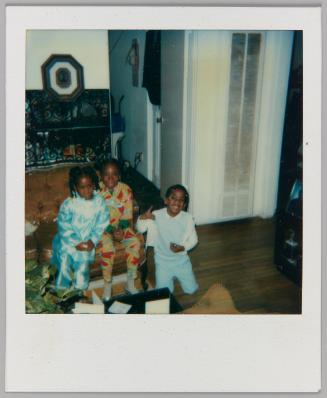 [Three children in pajama sets sitting on leather couch in living room]
