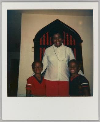[Woman wearing beads with arms around two boys at church]
