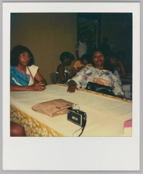[Two women seated with purse and camera on table]
