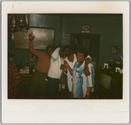 [Three men and a woman appear to be singing in home, man on left hold arm in the air]
