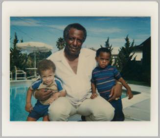 [Man seated at poolside with young boys in each arm]
