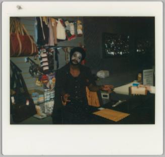 [Man with white face paint standing behind store counter]
