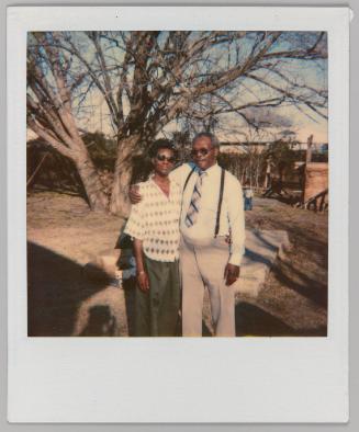 [Man and woman with arms around each other posing in wooded area with young boy in background]
